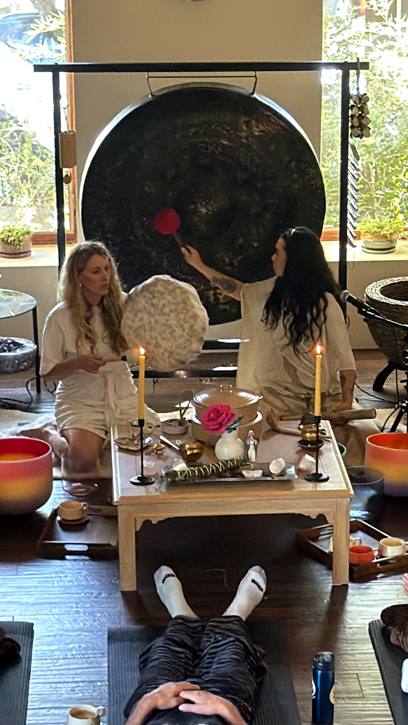 Two facilitators leading a candlelit sound ceremony before a large gong