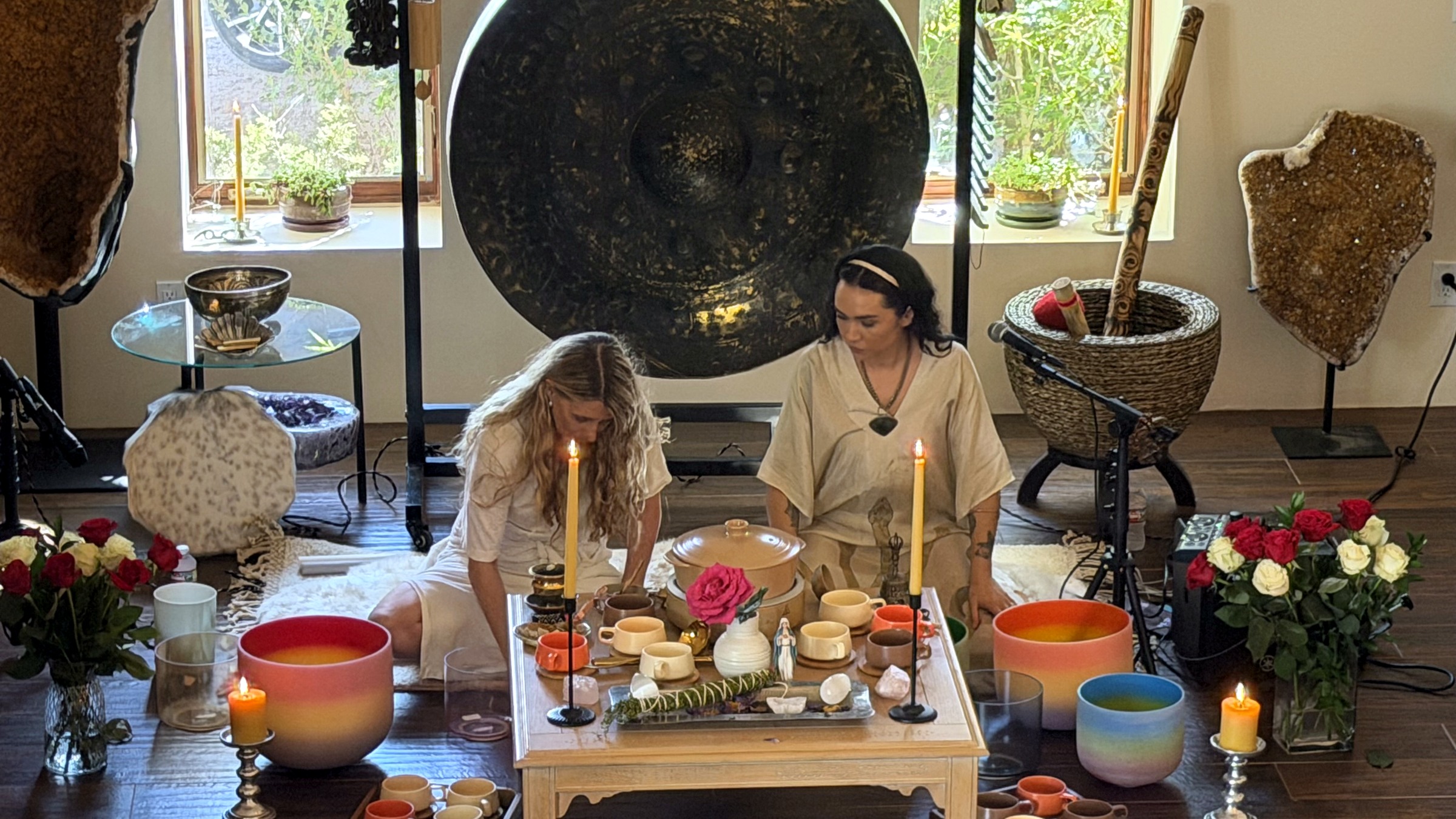 Facilitators seated at an altar surrounded by candles, flowers, crystal bowls, and a gong