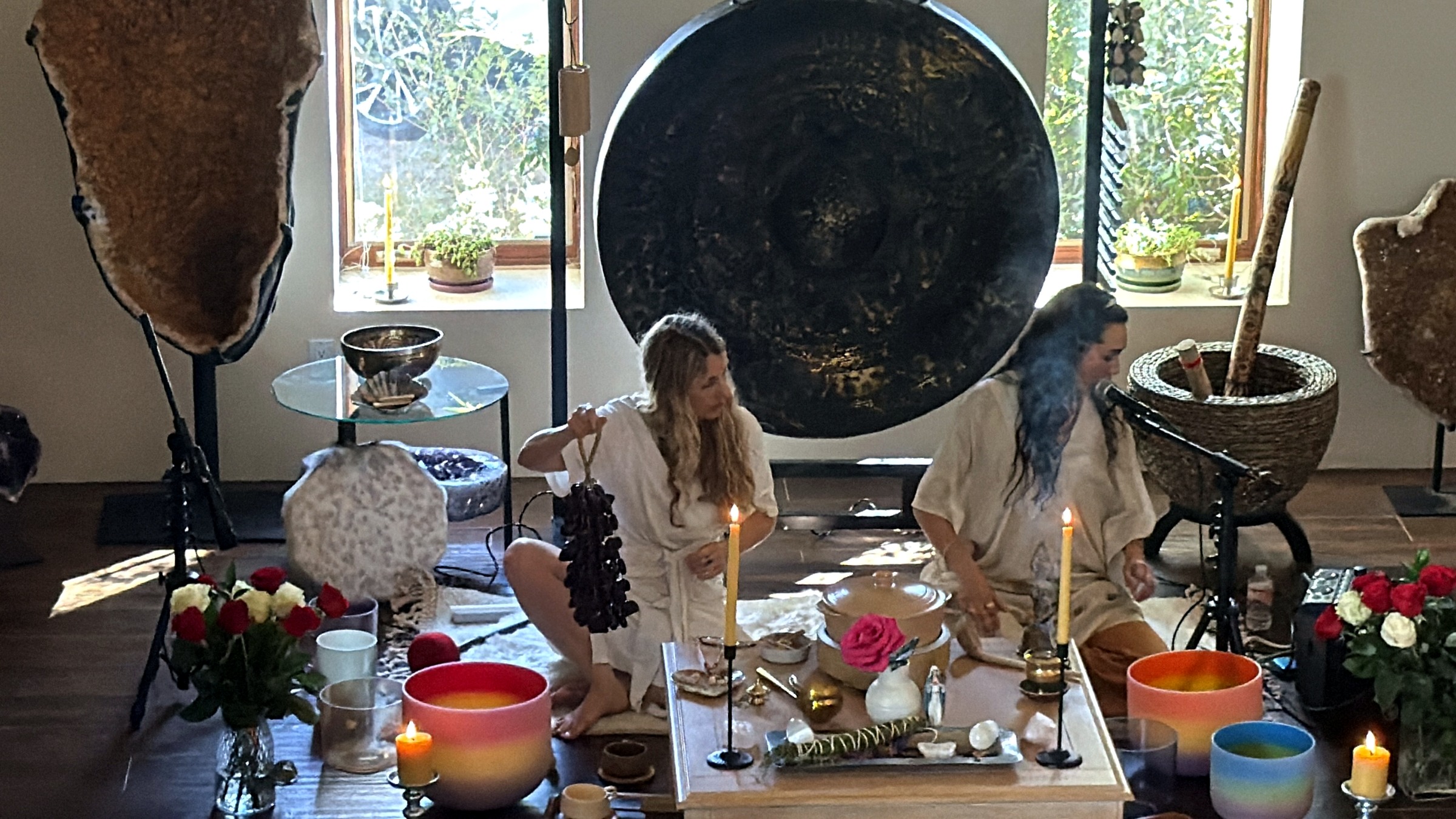 The two facilitators seated among the altar, flowers, bowls, smoke, and large gong